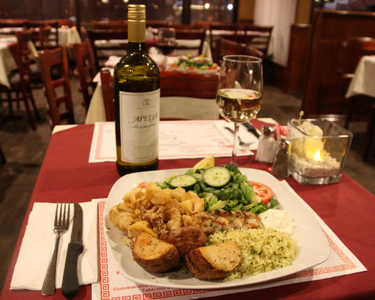 A table in the dining room: red tablecloth, Greek-key placemat, white wine and a full plate